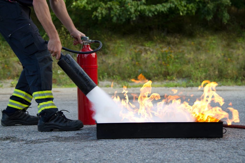 Instruktor, der anzeigt, wie ein Feuerlöscher bei einem Ausbildungsbrand verwendet wird
