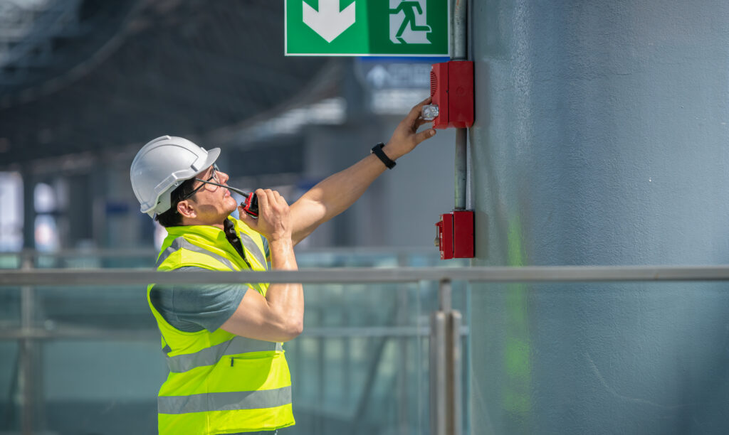 Ein Ingenieur in Schutzkleidung und mit Helm überprüft eine Brandstelle unter einem Schild für einen Flucht- und Rettungsweg